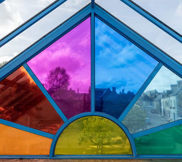 Un détail de l'oeuvre Newton de Richard Louvet qui représente une parties des fenêtres vitrées de formes géométriques de la salle des fêtes de Bazouges recouvertes d'adhésifs colorés transparents, de 7 couleurs différentes : rouge, orange, jaune, vert, bleu, indigo et violet.