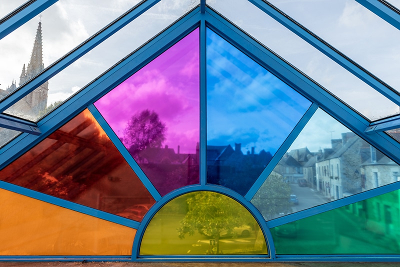 Un détail de l'oeuvre Newton de Richard Louvet qui représente une parties des fenêtres vitrées de formes géométriques de la salle des fêtes de Bazouges recouvertes d'adhésifs colorés transparents, de 7 couleurs différentes : rouge, orange, jaune, vert, bleu, indigo et violet.
